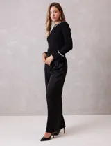 Pantalón palazzo de satén color negro, de tiro alto con pretina delantera estructurada, pasadores para cinturón y bolsillos laterales. Presenta una caída fluida y amplia, con elástico en la parte posterior de la cintura para mayor ajuste.