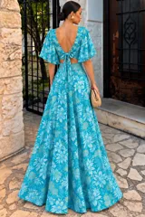 Vestido largo azul con estampado abstracto en tonos oscuros y detalles ornamentales en el escote en V y la cintura. Posee mangas amplias con volados y diseño fluido de gran movimiento.