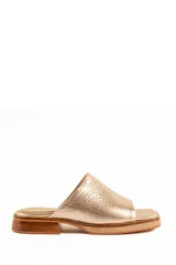 Zueco artesanal de cuero color dorado, con suela plana y taco bajo de madera con plataforma frontal.