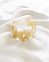 Pulsera dorada rígida con diseño de mariposas caladas.