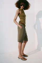 Bermuda fluida color verde militar con pinzas delanteras, tiro medio y trabillas en la cintura. Incluye un cinturón marrón de gamuza con hebilla metálica dorada.