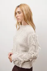 Buzo de punto color beige con cuello redondo, mangas largas con flecos decorativos y diseño de trenzas en el frente.