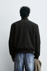 Cazadora bomber regular fit negra con cierre frontal de cremallera metálica, bolsillos de vivo en la cadera y acabados en rib elástico. El interior cuenta con efecto pelo.