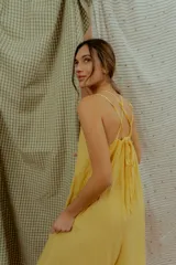 Mono largo de lino color amarillo, con escote en V, tirantes finos y detalles de costuras decorativas blancas en el escote y en los bajos de las piernas anchas.