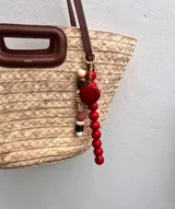 Colgante decorativo para bolso o llavero, compuesto por una cadena metálica con un conjunto de cuentas de diferentes formas, colores y texturas, incluyendo piedras naturales y cuentas de madera.