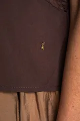 Blusa de algodón sin mangas en color blanco off-white, con cuello alto con volados y cierre frontal de cordones ajustables con lazos. Presenta detalles de encaje y bordados sutiles en la parte delantera.