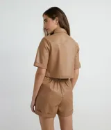 Camisa de manga corta confeccionada en cuero sintético color tostado, con cuello camisero, cierre frontal con botones en forma de corazón y dos bolsillos con solapa en el pecho.