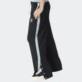 Pantalón deportivo Converse de corte ancho, color negro con franjas laterales en color celeste. Presenta cierre de botones a presión a lo largo de las piernas y logo de la marca bordado en la parte superior.