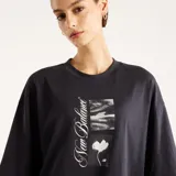 Remera oversize de color negro, confeccionada en algodón, con cuello redondo y mangas cortas. Presenta un estampado gráfico frontal con diseño abstracto en blanco y negro y la inscripción "New Balance".