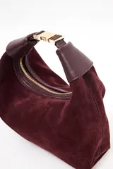 Cartera tipo hobo de Lolita, confeccionada en gamuza color bordó, con diseño de asa integrada y cierre superior. Presenta detalles en cuero liso en los extremos del asa y logo de la marca grabado en el frente.