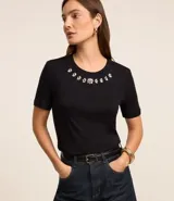 Blusa de manga corta confeccionada en viscosa, con cuello redondo decorado con apliques de brillos en forma de flores. Presenta un diseño básico y versátil.