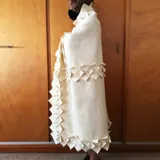 Manta de lana afieltrada color crema, con terminaciones decorativas de figuras geométricas.