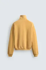 Sudadera de corte relajado confeccionada en algodón con interior de rizo, color amarillo mostaza con efecto lavado. Presenta cuello subido con cierre frontal de cremallera y detalle de cinta trenzada en el tirador, manga larga y acabados en rib.