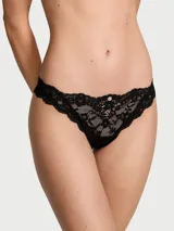 Panty tipo tanga de encaje negro con tiro bajo y detalle de pequeña roseta en el centro de la cintura.