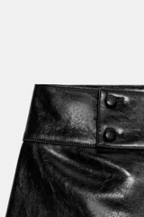 Shorts de tiro medio con efecto de cuero brillante en color negro, con cierre frontal y detalles de botones en la cintura.