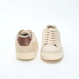 Zapatillas bajas color beige con textura, cordones y detalle marrón en el talón.