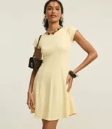 Vestido corto color amarillo pálido, con escote redondo y mangas cortas. Presenta recortes verticales en el torso que definen la silueta y una falda ligeramente acampanada.