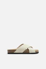 Sandalia abierta color crudo, fabricada en piel con acabado serraje. Presenta dos tiras anchas cruzadas en el empeine y plantilla con horma anatómica.