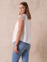 Blusa negra de crepe con apliques de crochet en los hombros. Tiene cuello redondo, mangas cortas y espalda con abertura ojal y botones.