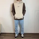 Canguro con capucha de diseño bicolor, combinando paneles en color blanco y beige. Presenta un bolsillo frontal tipo canguro y el logo de la marca bordado en el pecho.