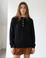 Buzo de punto negro con diseño geométrico calado, cuello redondo con abotonadura frontal parcial y mangas largas.