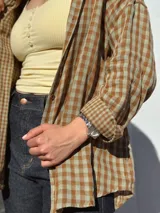 Camisa escocesa holgada, de manga larga, con estampa de cuadros en tonos de verde y marrón, y cierre frontal con botones.
