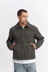 Campera de canvas color gris oscuro con cuello camisero, cierre frontal y bolsillo con cierre en el pecho. Presenta un diseño de estructura firme con estilo utilitario.