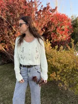 Saco tejido de punto color blanco marfil, con cuello redondo, cierre frontal con botones y bordados florales en el frente.