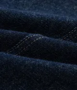 Pantalón de jean raw azul oscuro, corte barrel con piernas anchas y cintura cónica. Presenta costuras contrastantes, cierre tradicional con botón y bolsillos laterales.