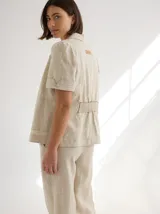 Chaqueta de lino color beige, con cuello camisero, manga corta y cierre frontal con botones de madera.