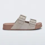 Sandalias Melissa modelo Cozy Slide M-Lover, en color beige con suela marrón. Presentan dos tiras superiores con hebillas ajustables y tiras de tela con la marca estampada.