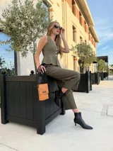 Phonebag pequeña color mostaza, confeccionada en cuero sintético, con solapa frontal y correa ajustable con logo de la marca.