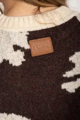 Sweater de punto con diseño combinado, presentando un estampado de manchas de vaca en el cuerpo y mangas con rayas horizontales en tonos azul y marrón. Posee cuello redondo y puños acanalados.