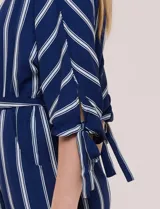Enterito largo de crepe color azul marino con diseño de rayas verticales blancas. Cuenta con escote redondo, mangas tres cuartos con detalles de lazos en los puños, cintura elastizada con lazo extraíble para ajustar, bolsillos laterales y pantalón de corte amplio.