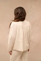 Camisa de broderie color blanco, con cuello redondo, cierre frontal con botones y mangas largas abullonadas con puños ajustados.