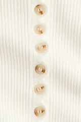 Saco corto en punto acanalado de color blanco, con cuello redondo y tapeta frontal con múltiples botones.