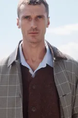 Trench de corte relajado con estampado de cuadros en tonos beige y marrón, cuello solapa en piel marrón, manga larga, bolsillos de vivo en cadera, cinturón ajustable y cierre frontal con botones.