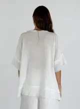 Blusa celeste de lino con escote en V y mangas cortas con volados. Tiene terminaciones desflecadas en el escote, mangas y ruedo.
