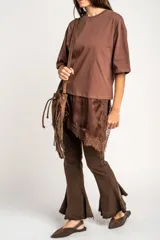 Remera oversize marrón con corte a la altura de la cadera, cuello redondo y mangas cortas holgadas. Incorpora un aplique inferior superpuesto de satén con detalles de encaje bordado en los bordes.