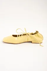 Chatitas de cuero color amarillo, con diseño acordonado en el empeine, puntera cuadrada y talón fruncido con cordón ajustable.