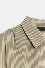 Camisa fluida de cuello solapa y manga corta, con diseño a rayas en tonos beige y blanco, detalle de pliegues en los hombros y cierre frontal con botones.