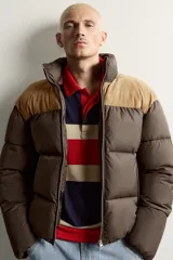 Cazadora puffer relaxed fit color marrón con canesú superior en tono tostado de acabado aterciopelado. Cuenta con cuello subido, manga larga, bolsillos de vivo en la cadera, acabados en elástico y cierre frontal con cremallera.
