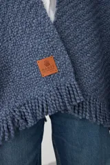 Ruana de tejido de punto grueso en color azul jean, con diseño abierto y terminaciones con flecos en el ruedo.