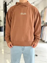 Canguro oversize color beige, con capucha y amplio estampado tipográfico en la espalda.