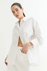 Camisa color crudo, de corte clásico, con cuello camisero, cierre frontal con botones y mangas 3/4 con trabillas.