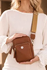 Bandolera pocket bag de cuero vacuno color suela, con bolsillo frontal con cierre y detalle de placa metálica con logo. Cuenta con correa de cinta ancha regulable y herrajes metálicos plateados.