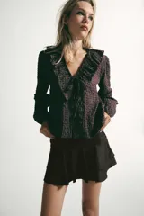 Camisa de manga larga con estampado de cuadros, escote en pico con volantes decorativos y cierre frontal con botones. Presenta puños elásticos.