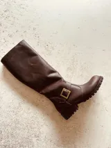 Bota de caña alta color marrón de cuero, con hebilla dorada y suela track.