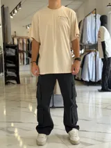 Remera oversize color beige, con diseño estampado en la espalda que incluye tipografía grande y texto descriptivo en negro.