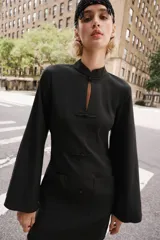 Vestido corto negro de cuello mao y escote en V, con mangas largas abanicadas y cierre de alamares en el frente. Cuenta con bolsillos frontales de plastrón y diseño de inspiración oriental.